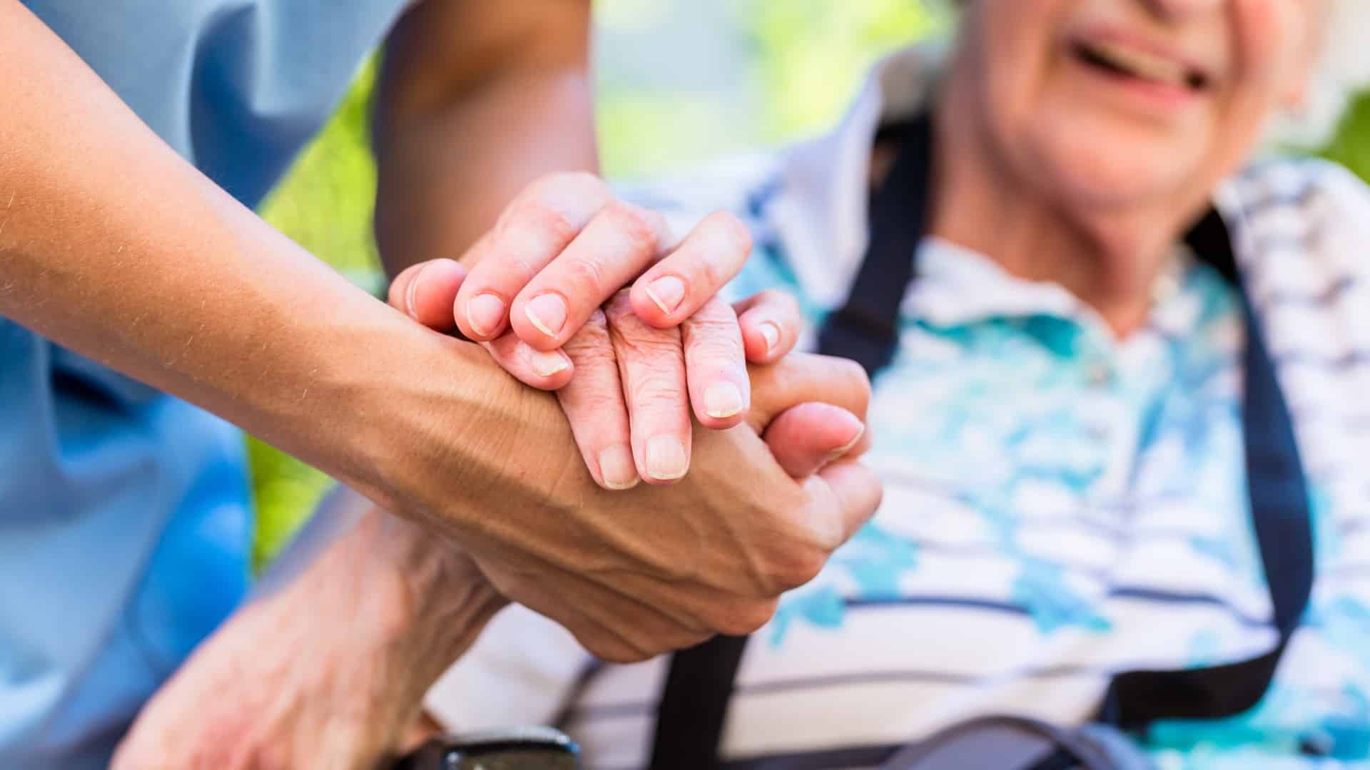 Gros plan sur les mains d'une aide soignante et d'une dame âgée