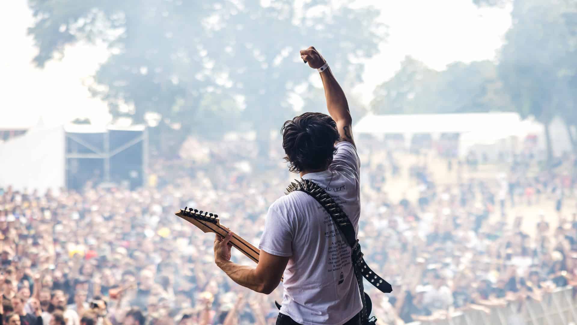 Guitariste lors d'un concert, guitare main gauche et poing droit levé face a la foule