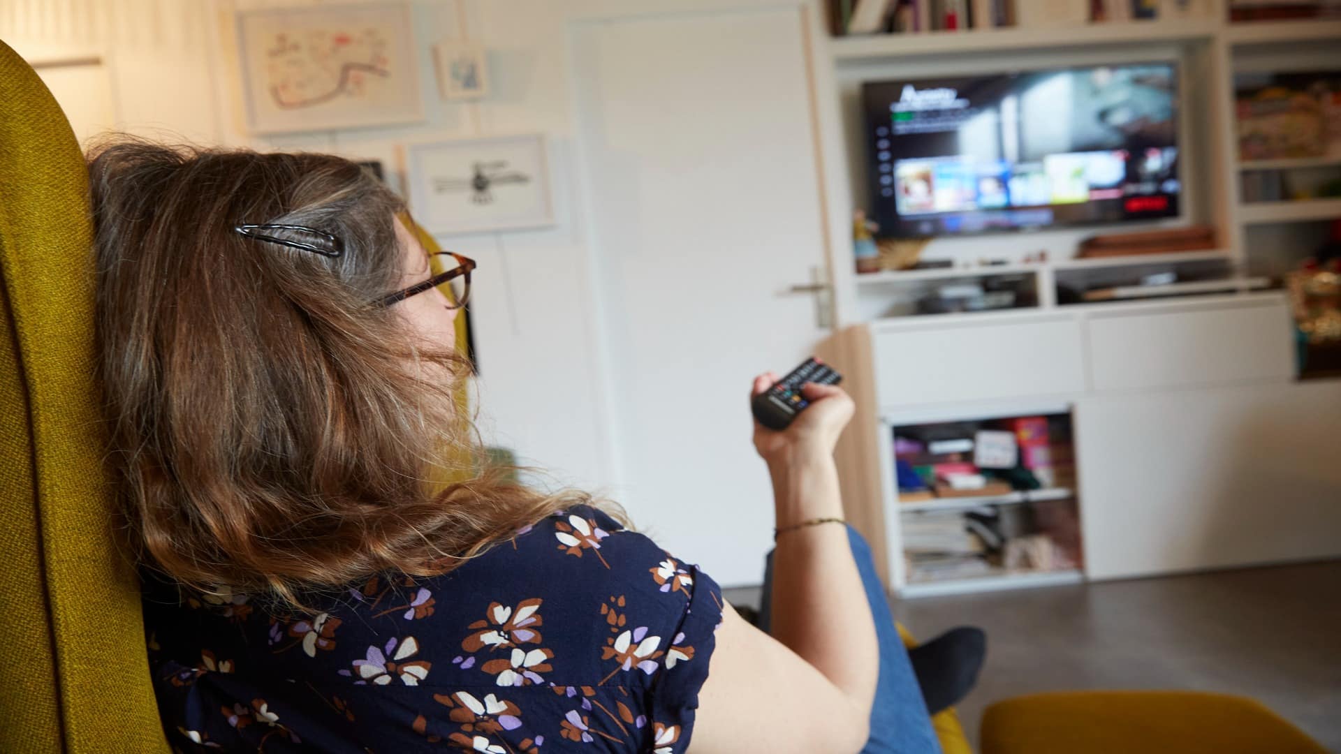 Femme assise dans un fauteuil et regardant la télévision, une télécommande à la main