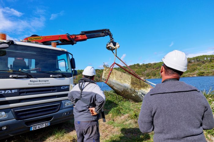 Deux hommes retirent une épave à l'aide d'une grue.