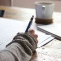 Une personne qui écrit sur un carnet en prenant un thé