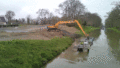 Un tractopelle extrait la vase transportée sur une barge, sur le canal et la dépose dans une vasière, lieu de stockage au bord du canal.