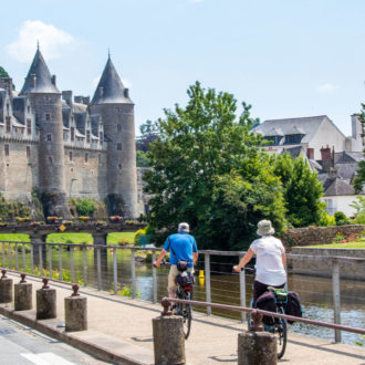 couple à vélo le long d'un canal passant à proximité d'un château (voir l'image en plus grand)