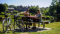 couple pique-niquant devant l'abbaye de Bon-Repos avec leur vélo à côté d'eux