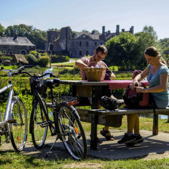 couple pique-niquant devant l'abbaye de Bon-Repos avec leur vélo à côté d'eux (voir l'image en plus grand)